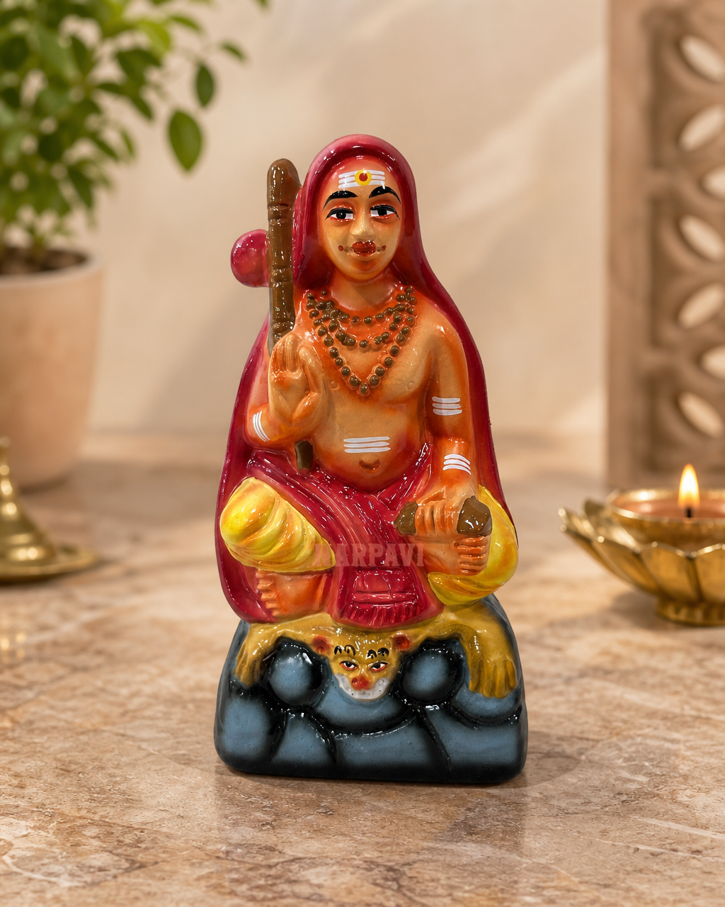 Adisankarar small statue in vibrant colors, placed on a table surrounded by decor items.