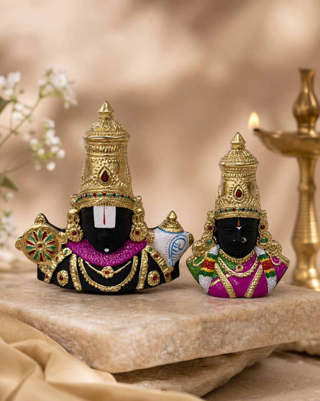 Detailed Balaji and Alamelu figurine set displayed on a stone surface with a gold oil lamp in the background.