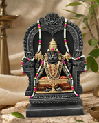 Elegant Yoganarasimha statue with intricate details, adorned with garlands, seated on a decorative throne, surrounded by foliage.