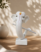 Elegant white elephant figurine with a flute on a wooden surface, surrounded by soft shadows and a ceramic vase.