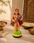 Colorful Puranthara Dasar figurine holding a musical instrument, surrounded by traditional decor.
