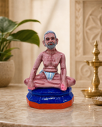A colorful figurine of Ramana Maharishi seated on a decorative base, ideal for home decor.