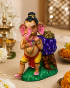 A colorful 13-inch statue of Ganesha carrying a vibrant purple sack, adorned with jewels, standing on a green base with two small animals at its feet, surrounded by traditional Indian decor elements.