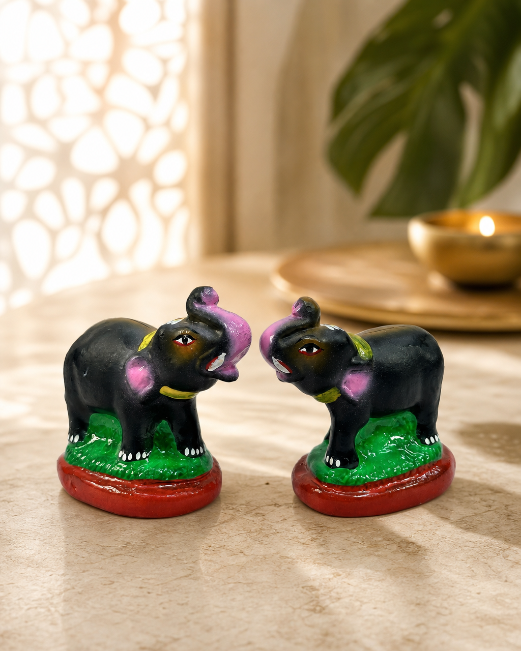 Pair of small black elephant figurines with pink and green accents placed on a decorative surface