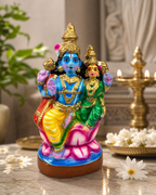 Colorful Lakshmi Narayanan idol on a decorative surface with flowers and a diya in the background