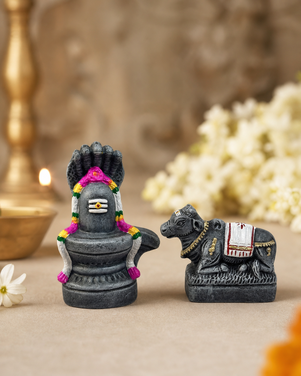 Decorative Lingam and Nandi figurine set on a table with candles and flowers in the background.