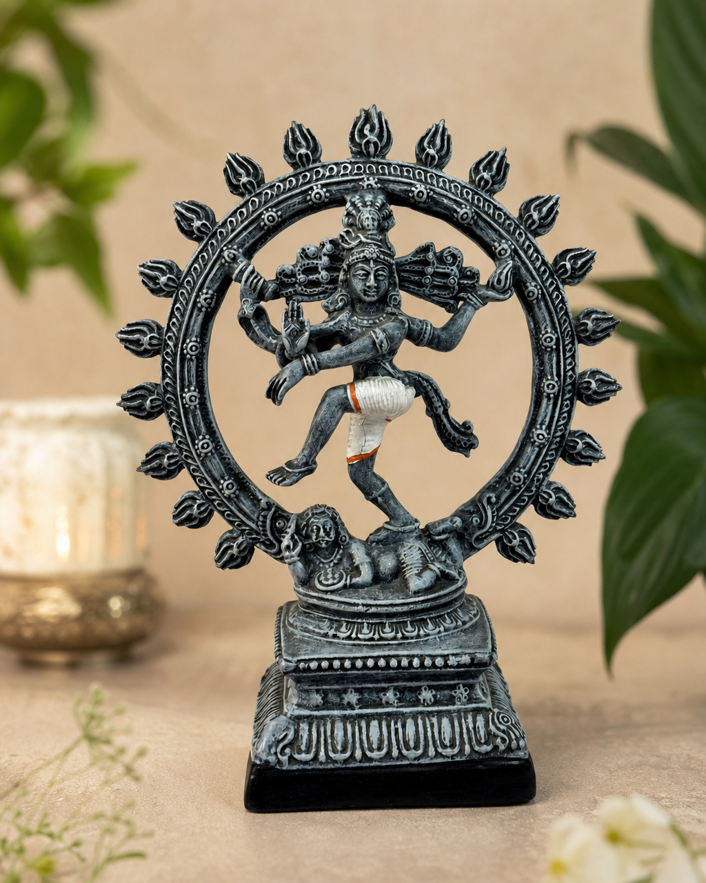 Elegant black Natarajar statue on a decorative base with intricate details, surrounded by foliage.