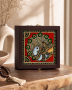 Decorative box with colorful peacock artwork on a wooden table with a vase in the background.