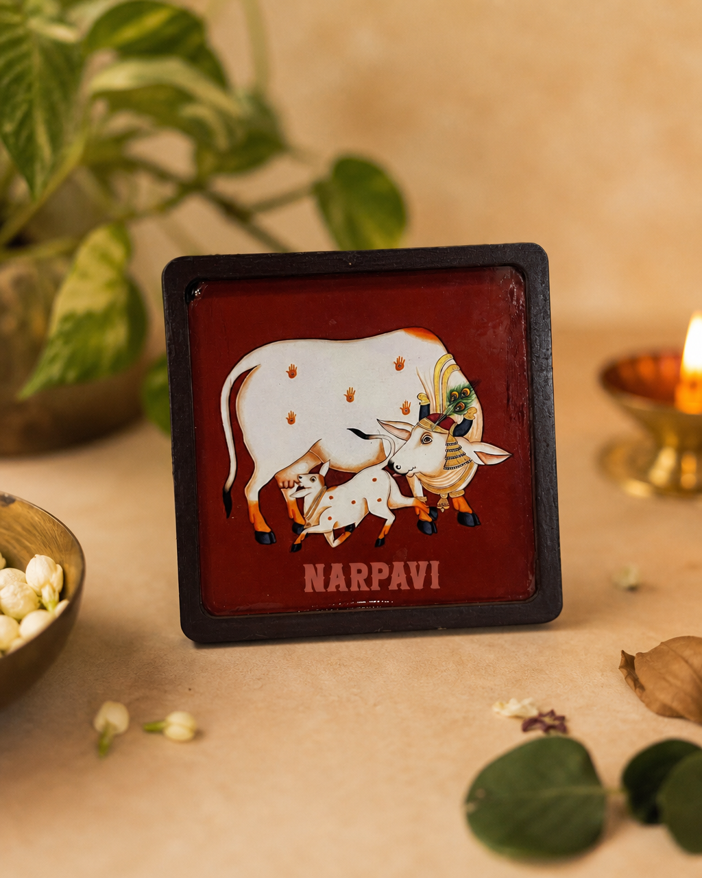 Square magnet with a traditional cow and calf design, placed on a beige background next to a candle and leaves.