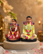 Colorful Pen Maapilai figurine set depicting a traditional couple sitting, surrounded by candles and petals.