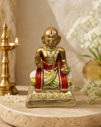 Desigar idol in traditional attire on display with flowers and a lamp in the background.